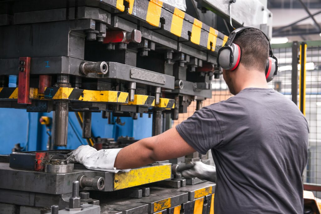 Worker in a factory operating machinery wearing hearing protection and gloves.